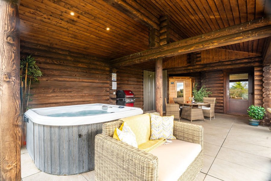 Covered outdoor terrace at Melody lodge with hot tub, dining table, barbecue and sauna.