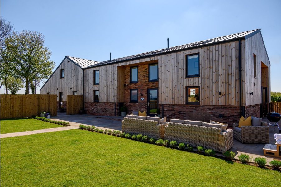 Exterior of Wheatsheaf Barn, modern countryside holiday home with wooden cladding, patio seating, and private hot tub.