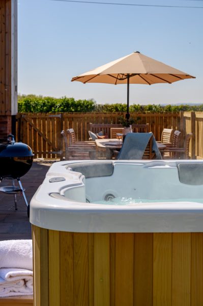 Wheatsheaf Barn private outdoor hot tub with patio dining area, barbecue, and parasol.