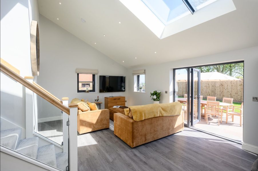 Field Cottage open-plan living room with skylight, sofas, and doors leading to outdoor dining area.
