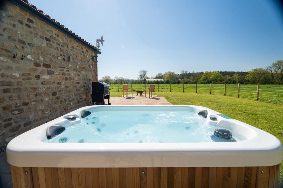 Luxury, outdoor hot tub with robes at Whitwell Nook in North Yorkshire with enclosed stone patio garden.