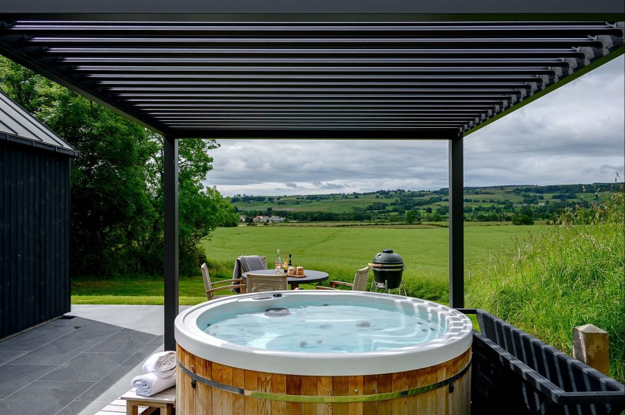 Private outdoor hot tub at Ake lodge in North Yorkshire overlooking rolling countryside views from a covered terrace.