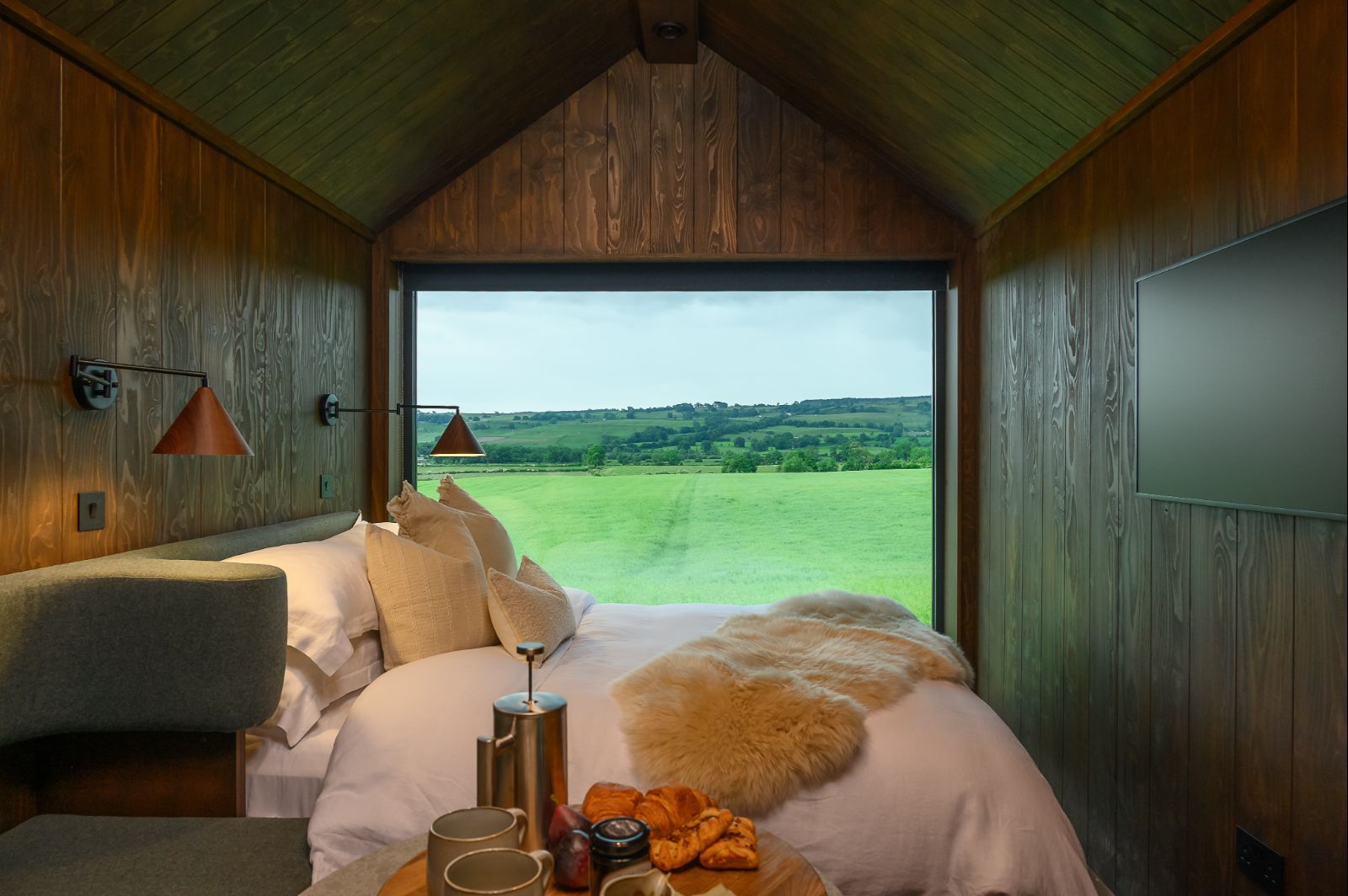 Luxury studio bedroom in Elvar Lodge, North Yorkshire, featuring panoramic countryside views through a floor-to-ceiling window.