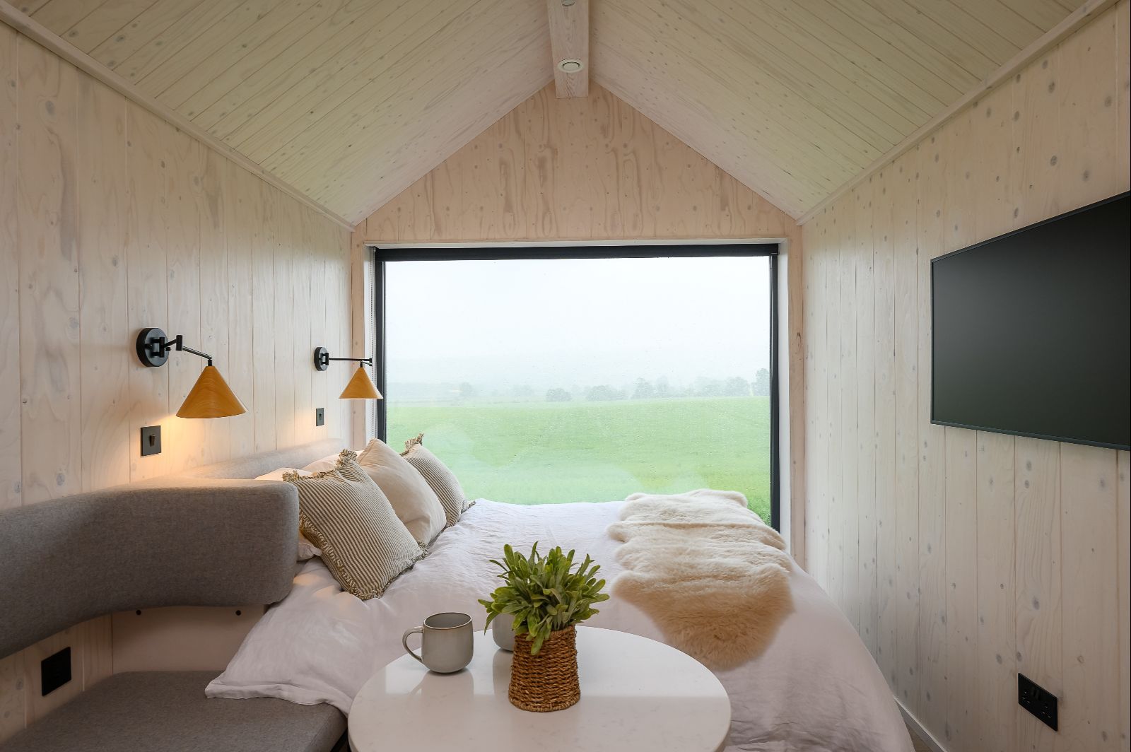 Luxury lodge bedroom with king-size bed and panoramic Yorkshire countryside views through a floor-to-ceiling picture window.