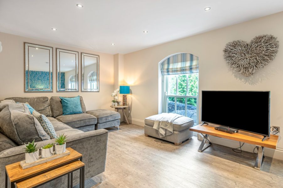 Comfortable living area with corner sofa, smart TV, large mirrors and window overlooking greenery.