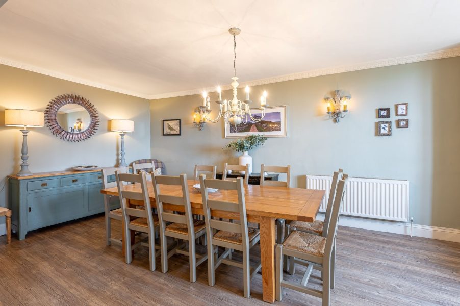 Dining room at 30 Frenchgate with a long wooden table and chairs, chandelier, wall lights, and a sideboard with lamps and mirror.