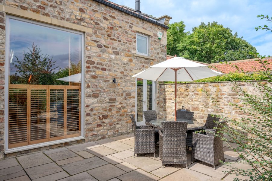 Stone-built holiday cottage patio with outdoor dining table, parasol and enclosed garden space at Georgia cottage near Richmond.