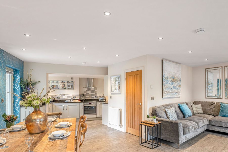 Bright open plan living, dining and kitchen area with large wooden table, modern kitchen and comfortable corner sofa.