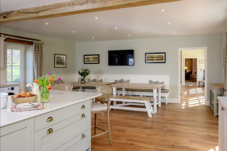 Open-plan kitchen and dining area in Hollins Barn with large island, wooden dining tables and bench seating.