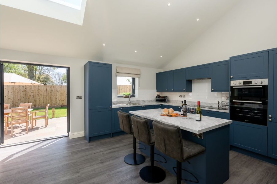 Field Cottage kitchen with blue cabinets, island seating, and doors opening to garden patio.