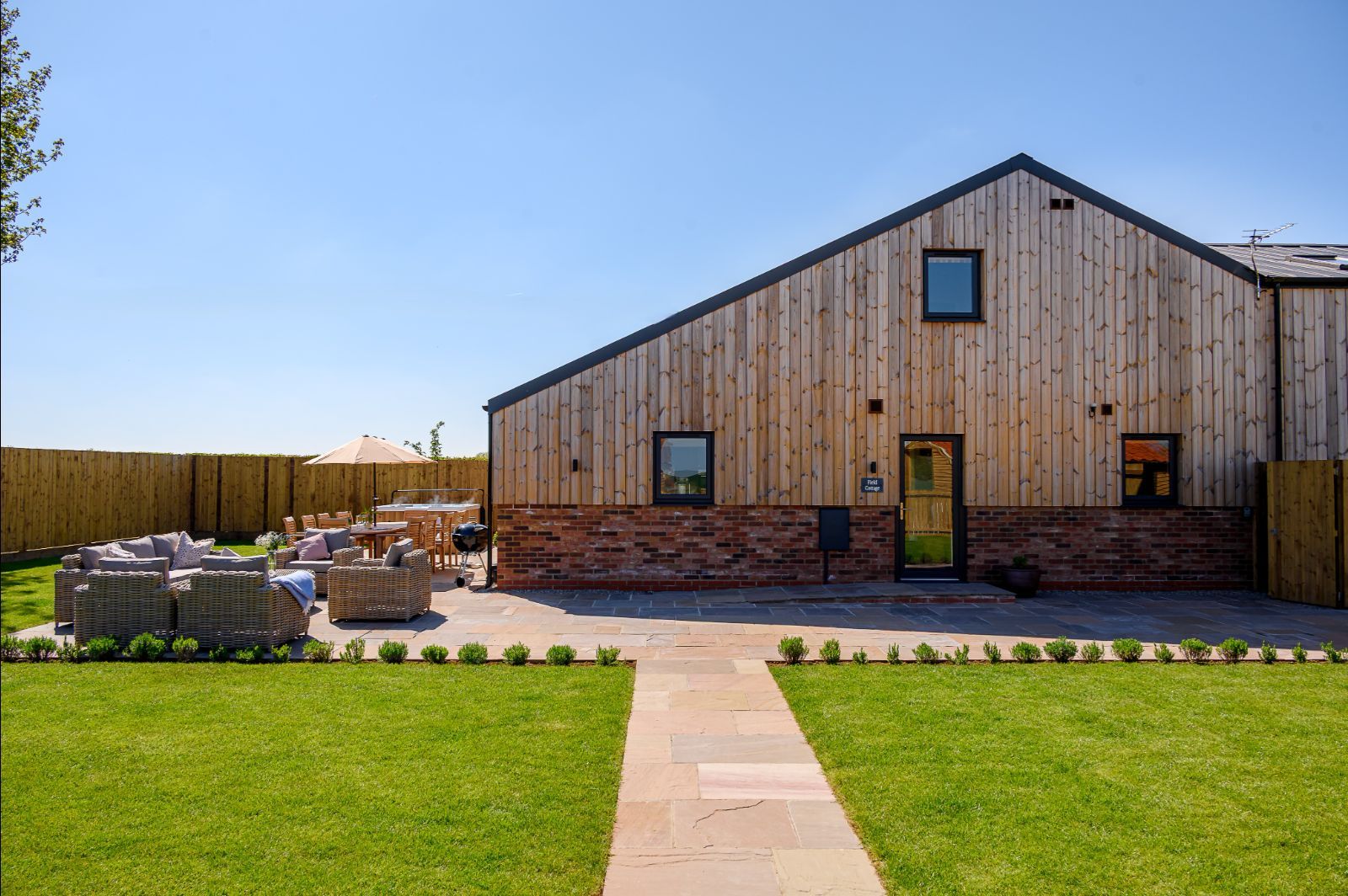 Field Cottage rear exterior with lawn, patio, outdoor dining, and wooden barn-style design.