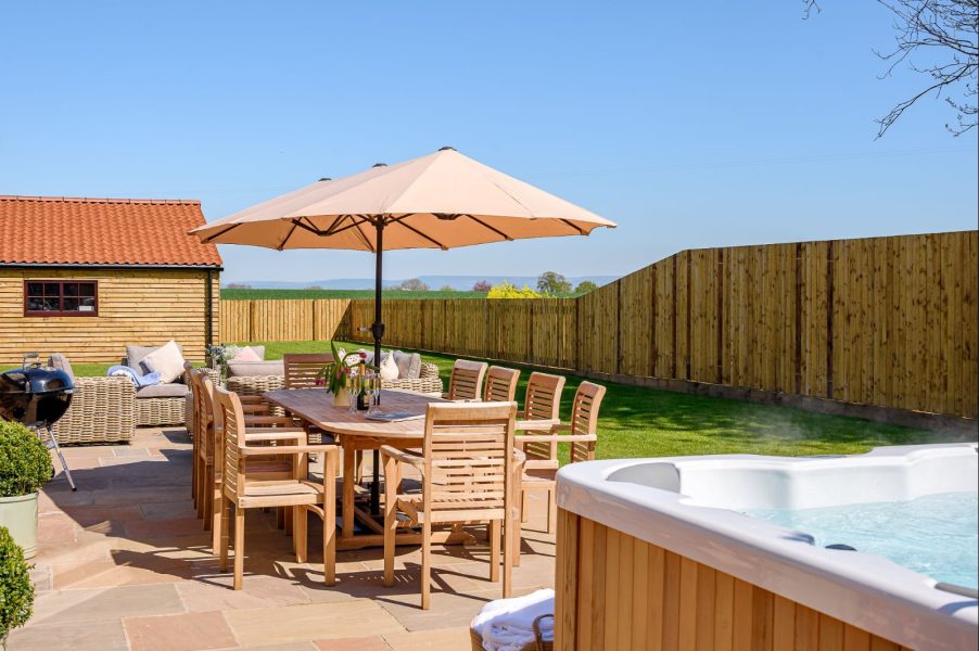Field Cottage patio with hot tub, outdoor dining table, parasol, barbecue and cushioned seating.