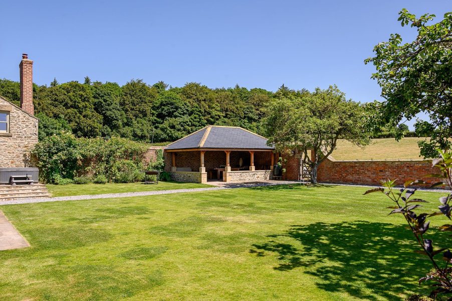 Garden at Hollins Farmhouse in the Yorkshire Dales with a spacious lawn, covered outdoor dining area and surrounding countryside.