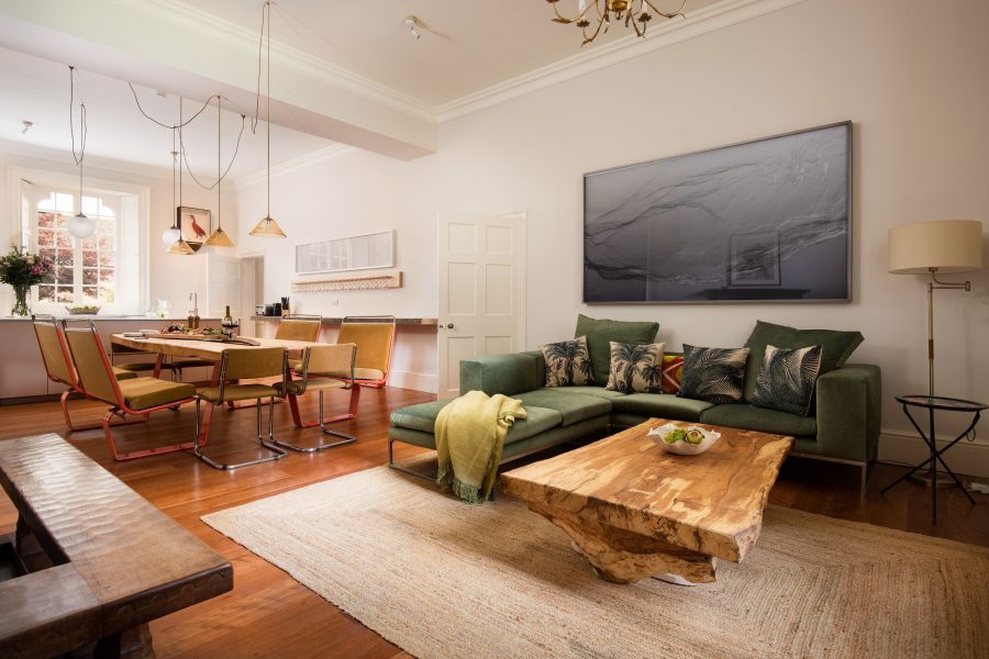 Open-plan living and dining area at Aquarius Rising with a green corner sofa, wooden coffee table, and dining table beneath pendant lights.