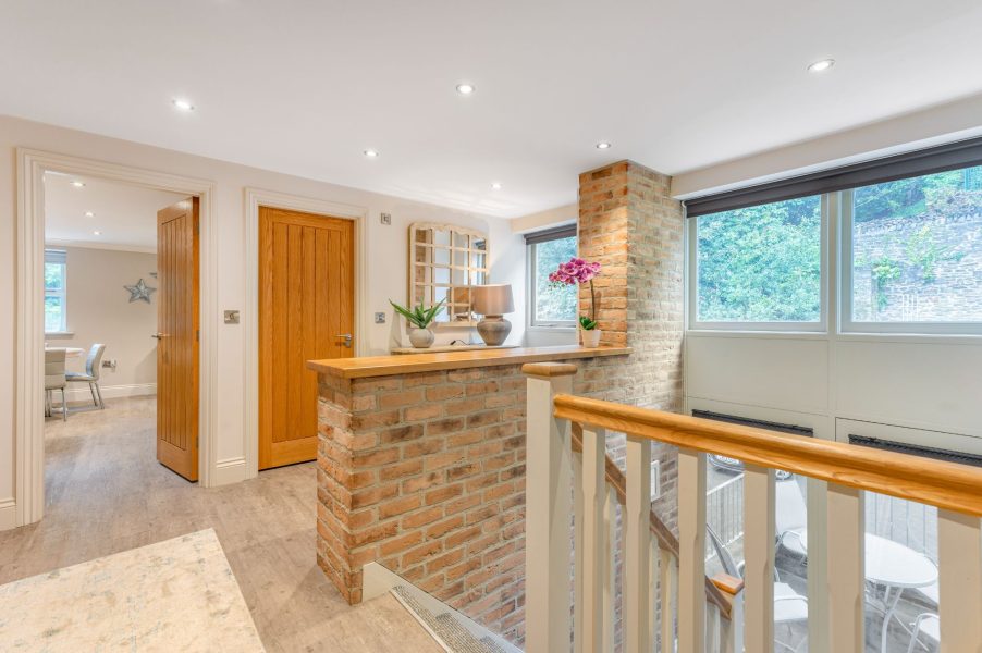 Landing area with exposed brick feature and large windows at Darcy Mews home