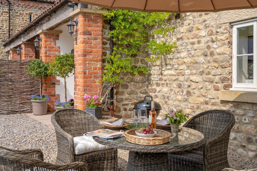 Outdoor patio dining area with BBQ and rustic stone walls at Feathered Nest holiday cottage