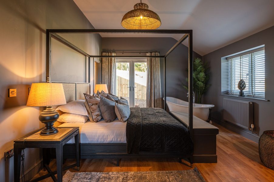Bearskin Bedroom with a four-poster bed, bedside lamp, French doors, and a freestanding bath by the window.