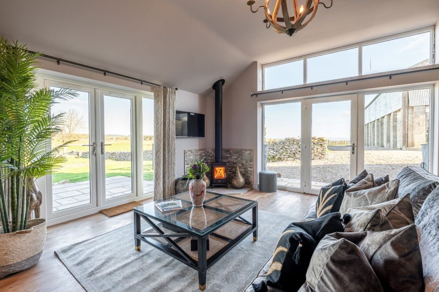 Living room at Bearskin with a sofa, glass coffee table, wood-burning stove, and two sets of French doors.