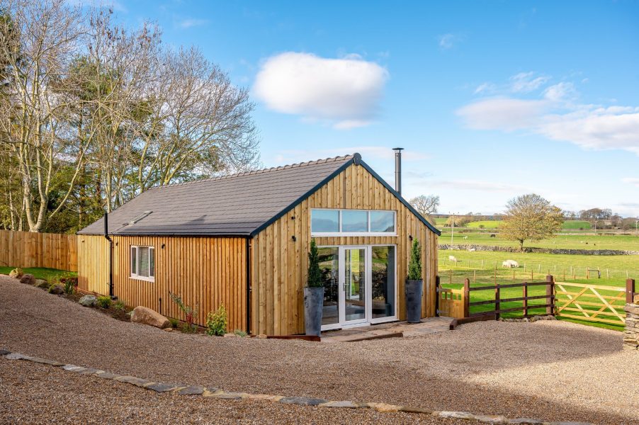 Bearskin exterior view with timber cladding, glass doors, and a gravel driveway leading to the entrance.
