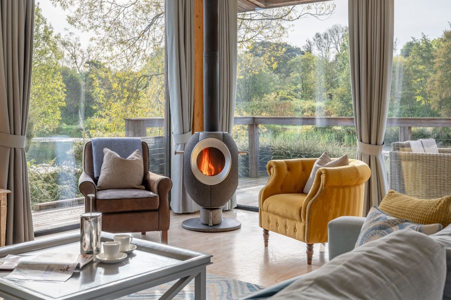 Living area in Jasper lodge with sofas, armchairs, wood-burning stove and lake views.