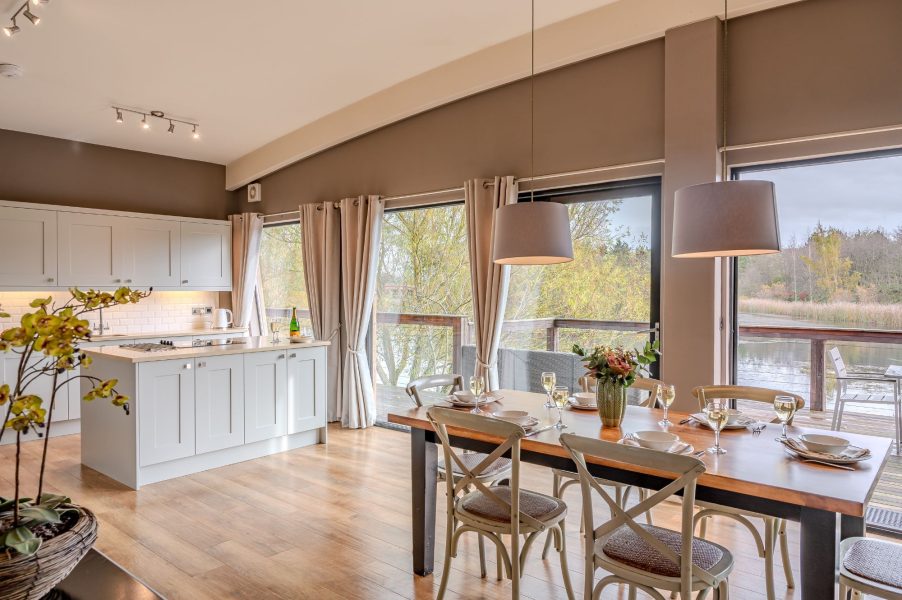 Open-plan kitchen and dining area in Flora lodge at Brompton Lakes with large table and sliding doors to private lakeside decking.