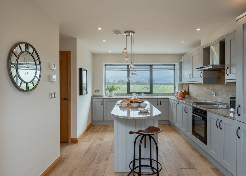 Ellesmere Barn modern kitchen with central island, breakfast seating and countryside views through large window.