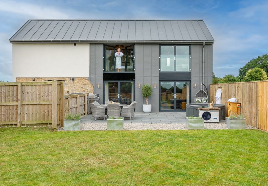Exterior view of Ellesmere Barn, a holiday cottage with private garden, patio seating and balcony above.