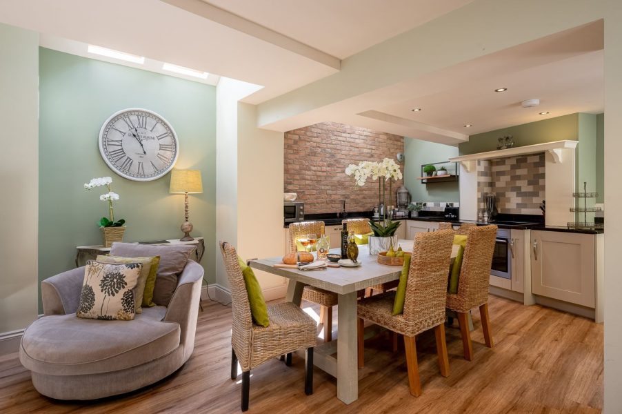 Darcy Mews open-plan kitchen and dining area with skylights, exposed brick wall, modern fitted kitchen, and dining table with wicker chairs, styled with soft green tones and cosy seating area.