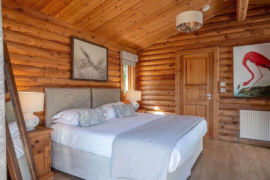 Master bedroom in William lodge with king-size bed, upholstered headboard and wooden log walls.