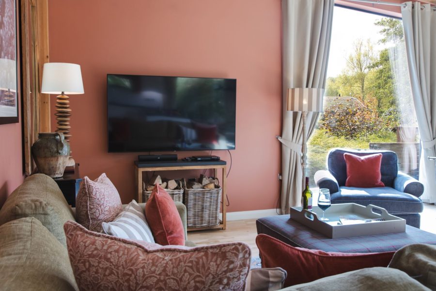 Comfortable lounge at Cara lodge with cosy seating, wall-mounted TV and large windows at Brompton Lakes, Yorkshire.