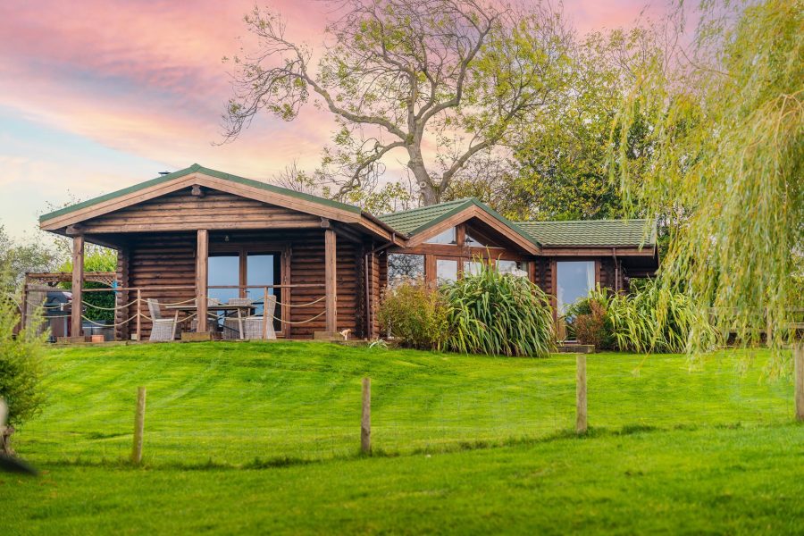 Exterior of William lodge, log cabin at Sun Hill Lodges surrounded by green countryside and landscaped garden.