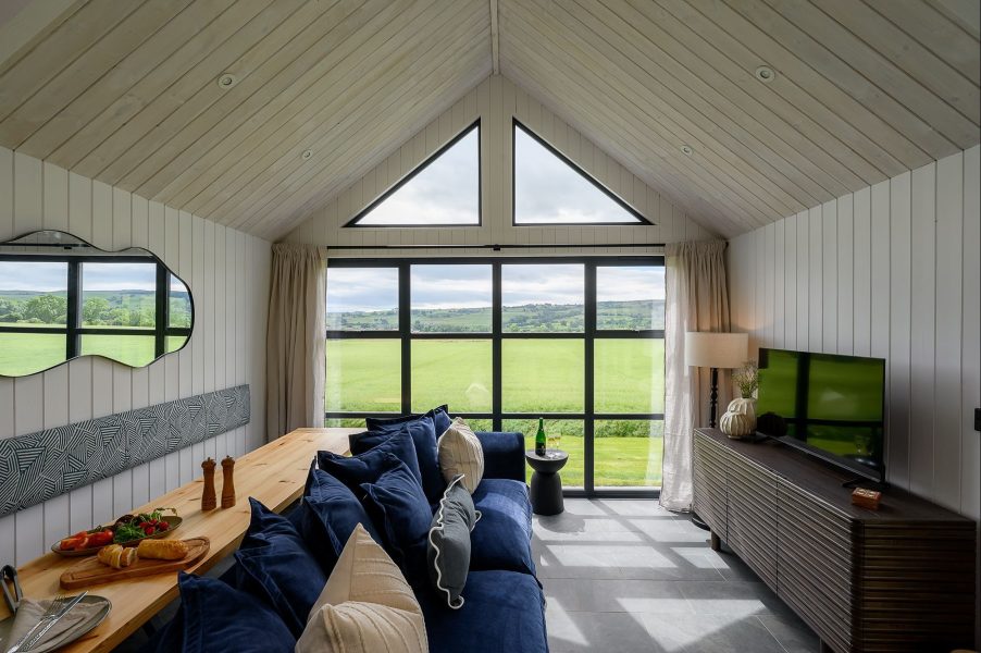 Open-plan living area at Freyja lodge in North Yorkshire with floor-to-ceiling windows overlooking rolling countryside views.