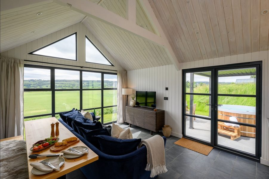 Open-plan living area at Freyja lodge in North Yorkshire with floor-to-ceiling windows and access to a private patio with hot tub.