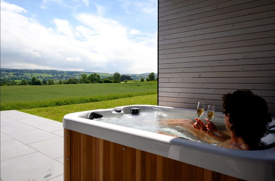Guests relaxing in a private hot tub on the covered terrace of a luxury lodge at Greenbank Lodges.