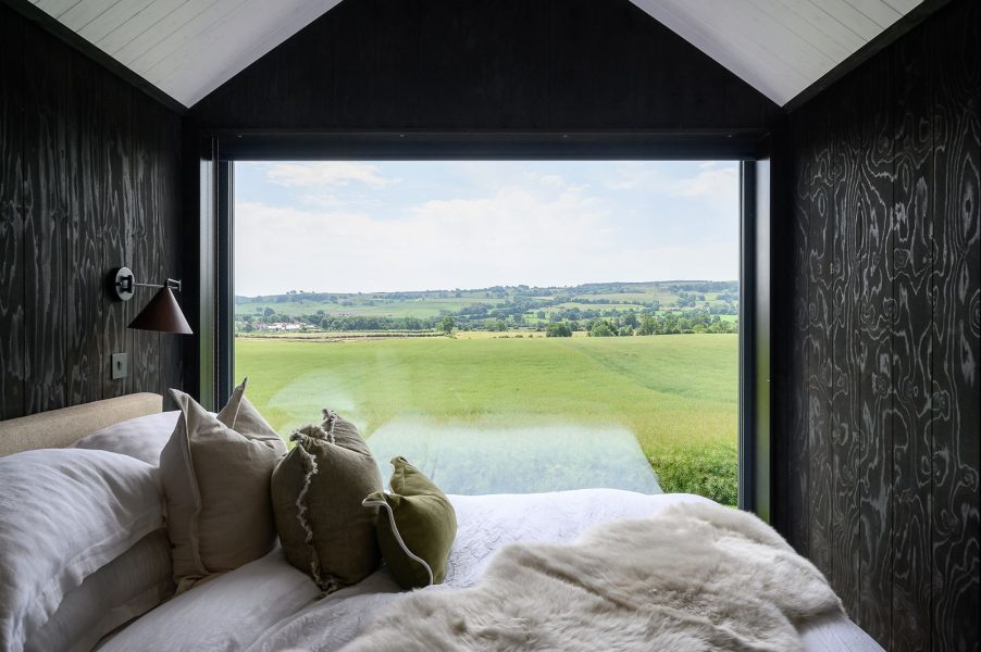 Bed positioned beneath a large gable window overlooking rolling Yorkshire countryside