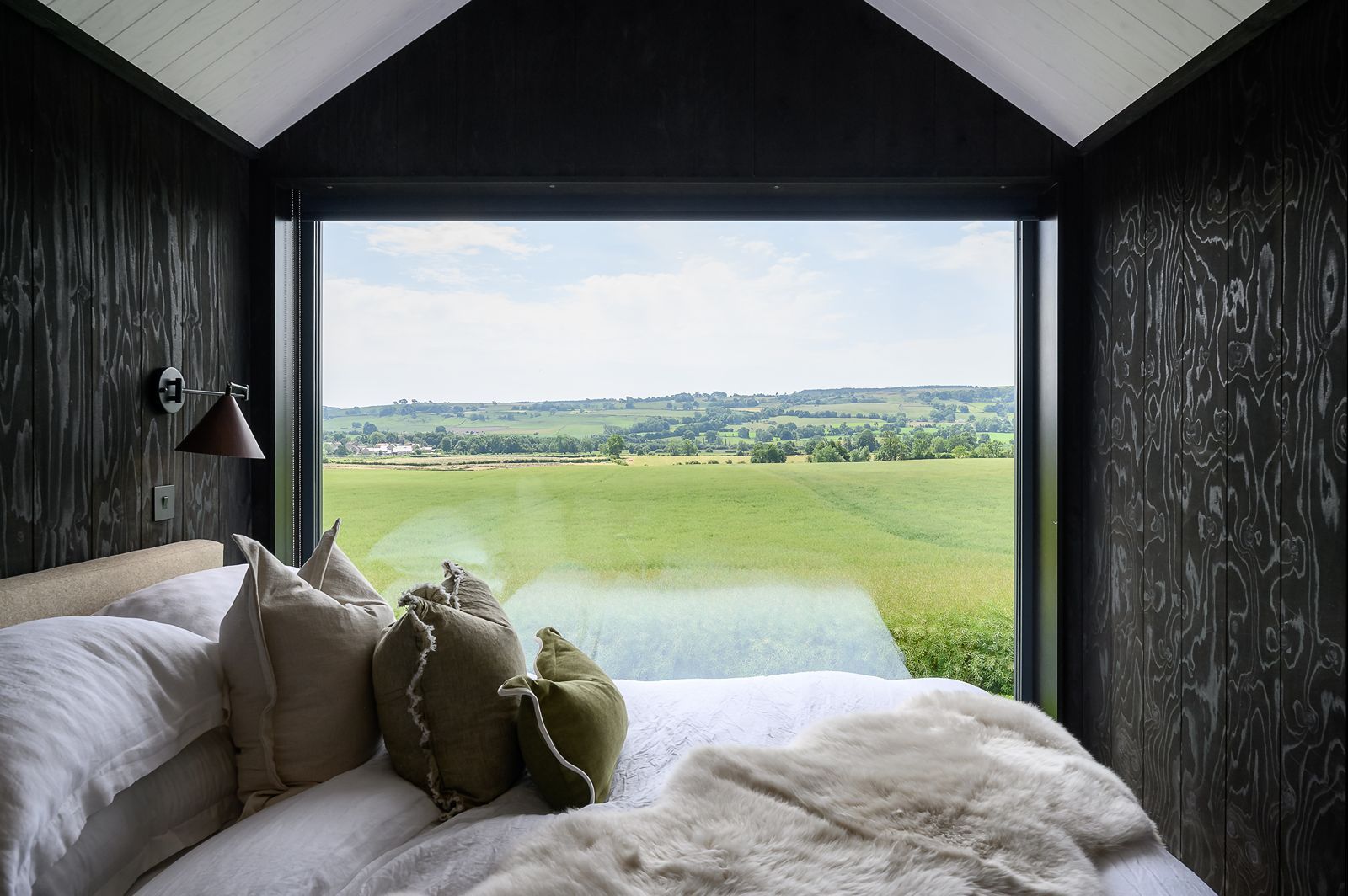 Bed positioned beneath a large gable window overlooking rolling Yorkshire countryside