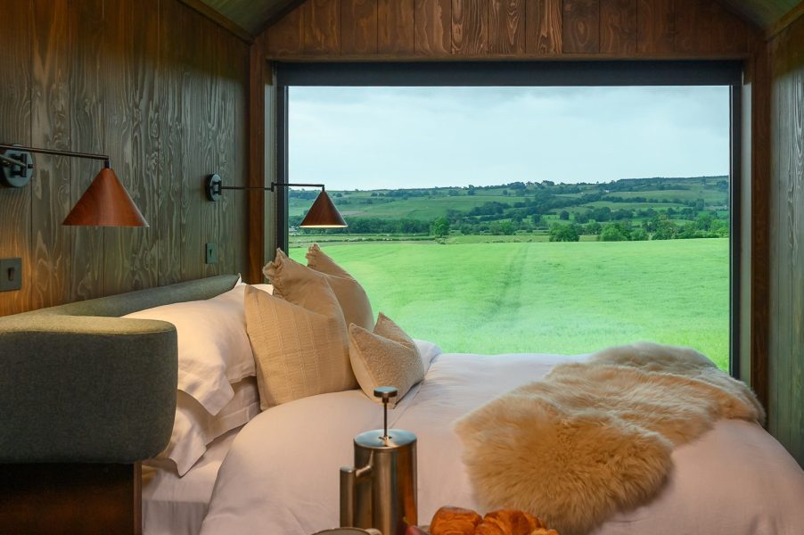Luxury lodge with king-size bed and panoramic Yorkshire countryside views through a floor-to-ceiling window.