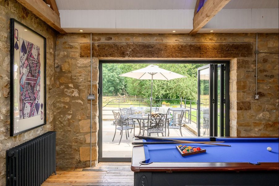 Games room in Kingfisher holiday cottage with pool table, bar area, exposed stone walls and vaulted beams.