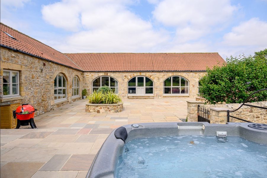 Luxury hot tub in private courtyard at Kingfisher cottage with surrounding stone buildings.