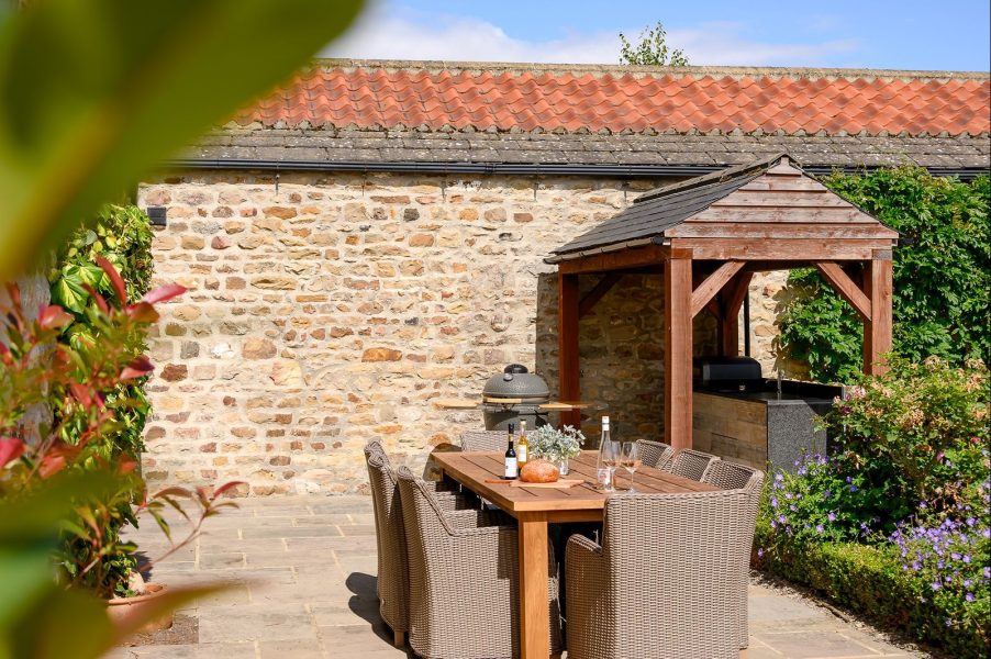 Sunny patio with outdoor dining set, parasol and stone wall at Henry cottage.