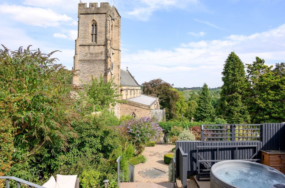 Courtyard patio at 30 Frenchgate with a hot tub, outdoor sofa seating, and a stone building with bay windows and steps up to a terrace.