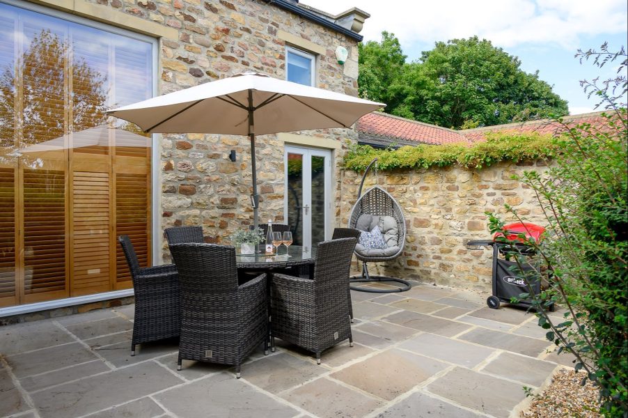 Stone-built holiday cottage patio with outdoor dining table, parasol and enclosed garden space at Georgia cottage near Richmond.