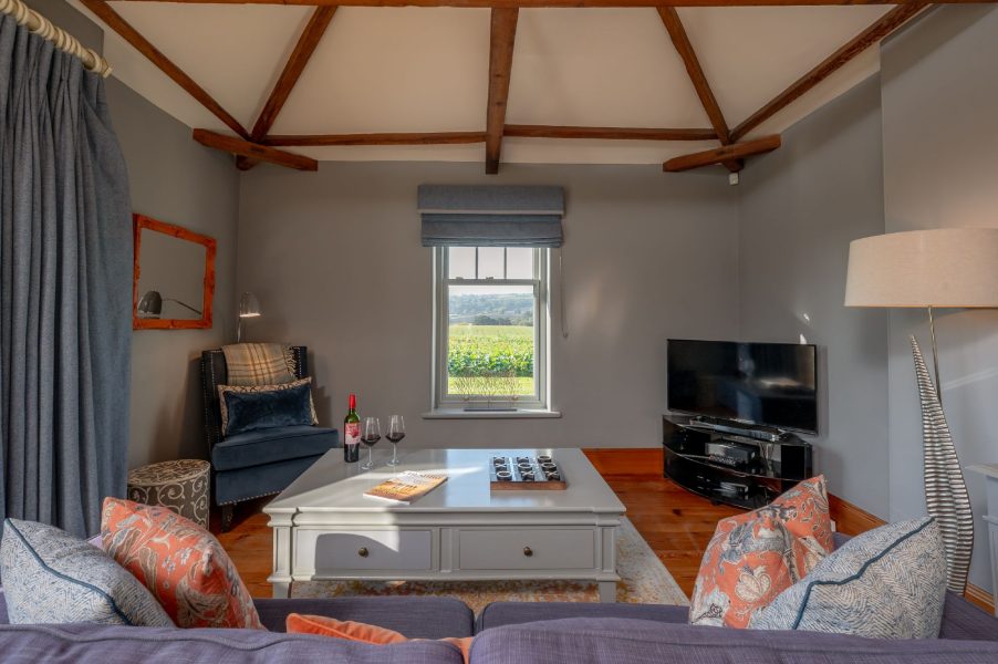Cosy living room at Wayside Cottage with exposed wooden beams, comfortable seating, TV, and countryside views through the window.