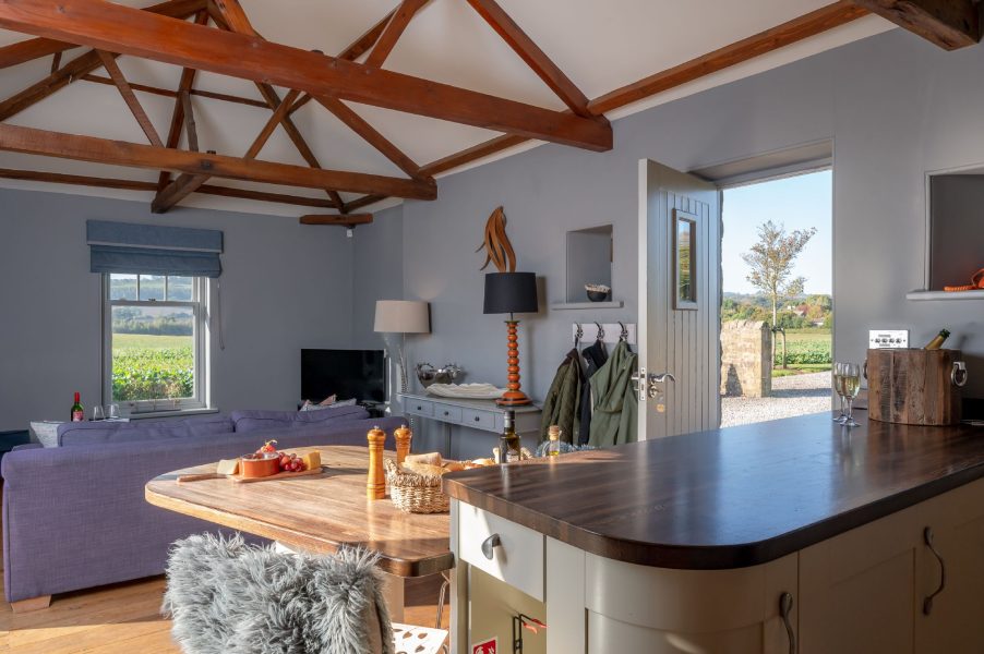 Open-plan kitchen and living area at Wayside Cottage featuring a wooden island, dining space, and doors opening to scenic rural surroundings.