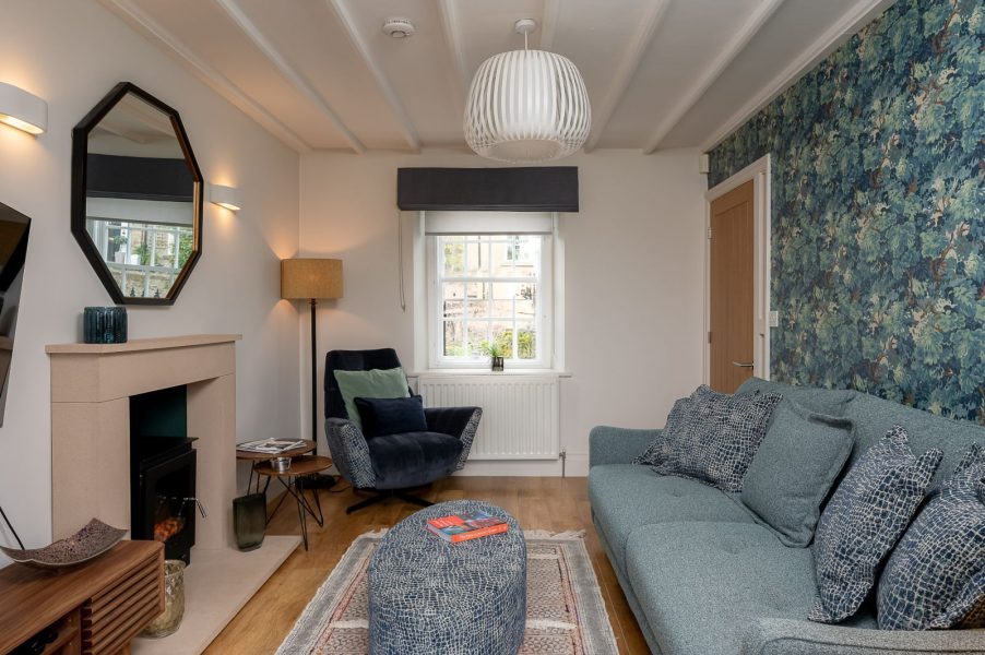 Maison Cottage living room with cosy sofa, armchair, fireplace and feature wallpaper with soft lighting