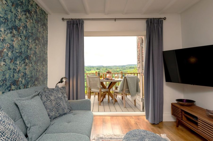 Maison Cottage living room with sofa and open doors leading to a balcony with outdoor dining table and countryside views