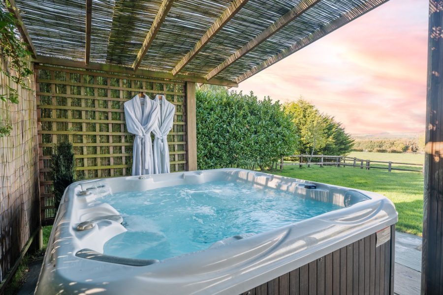 Private outdoor hot tub under canopy at Woodlands log cabin with robes and garden setting