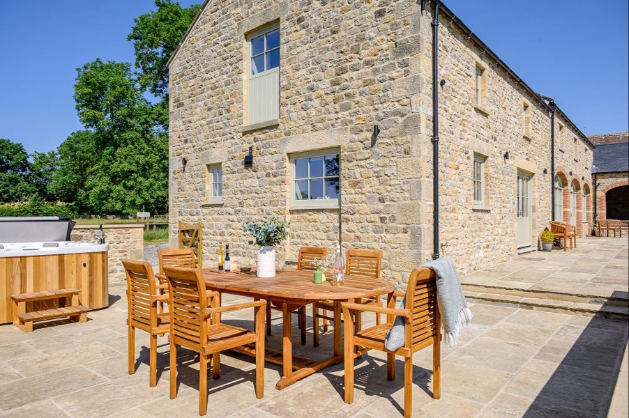Private stone terrace at Hollins Barn with outdoor dining furniture, hot tub and spacious patio.